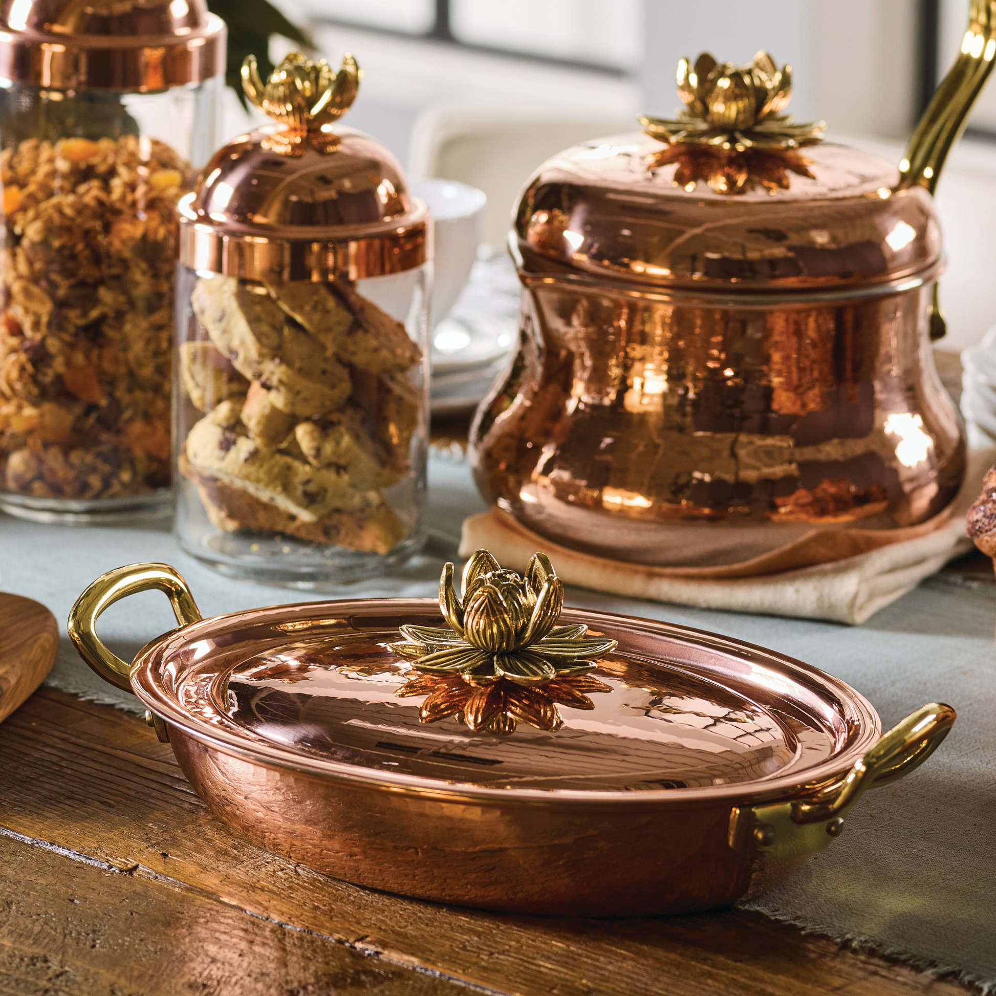 Hammered copper 10" covered oval gratin, tin-lined by hand over fire, with bronze handles. Shown with matching tea kettle and Lotus glass jars from the Glamstore Historia collection