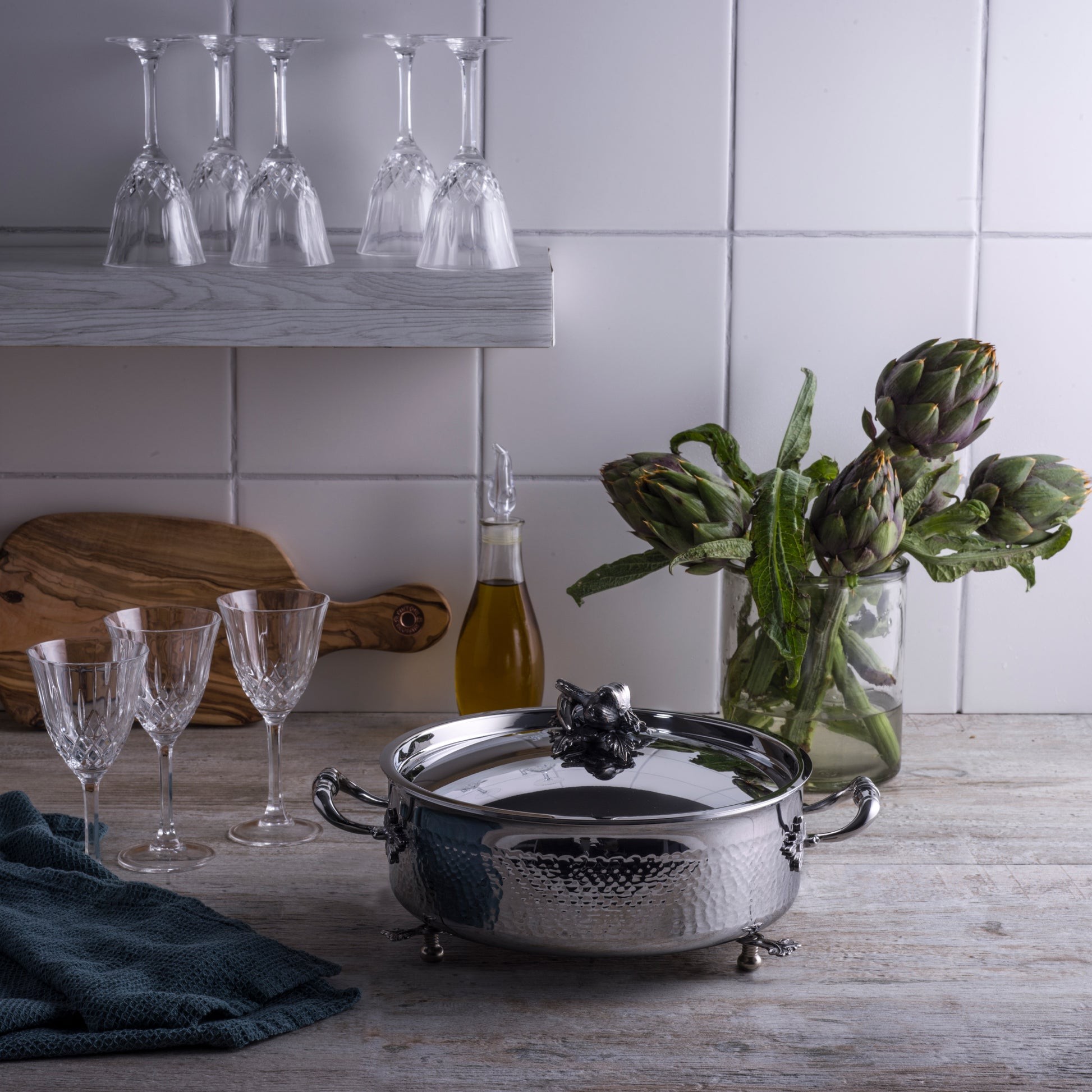 Opus Prima hammered clad stainless steel braiser with decorated silver-plated lid knob finial  an Italian kitchen with glass and artichokes